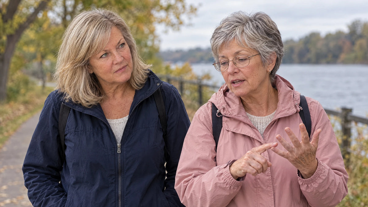 Diane listening closely as her friend Ruth counts something off on her fingers on a riverside walk
