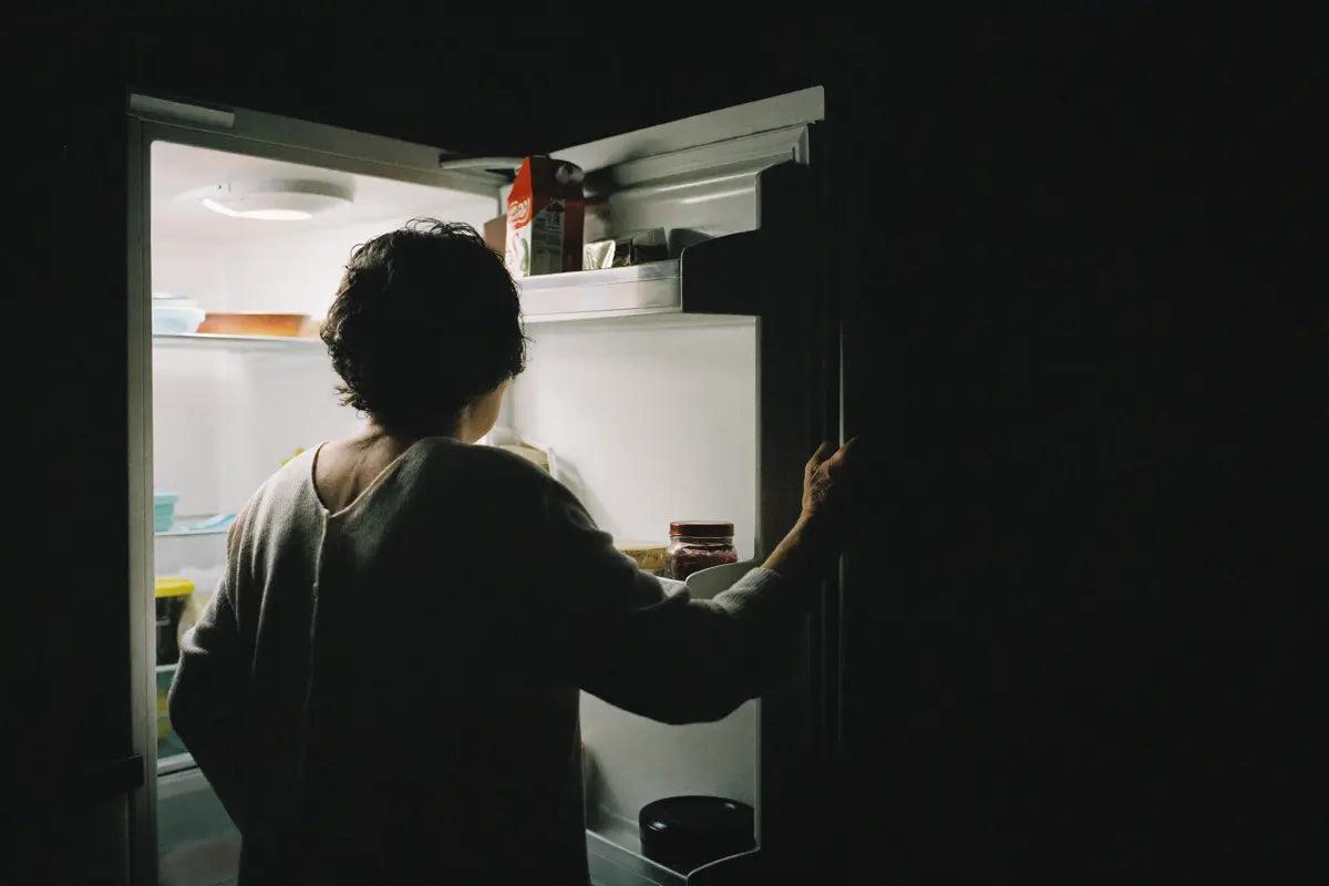 A woman standing at an open refrigerator in a dark kitchen