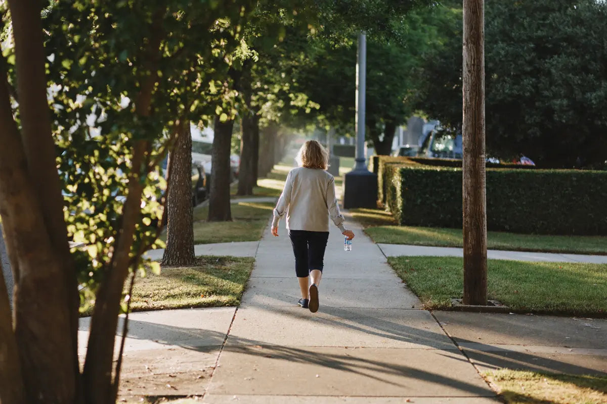 A woman walking on a tree-lined sidewalk in the morning